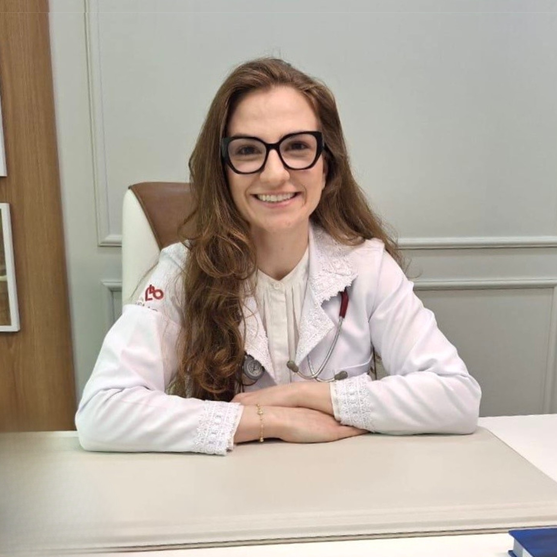 Dra. Laura Orlandini Lodi sorrindo, de jaleco branco, em seu consultório