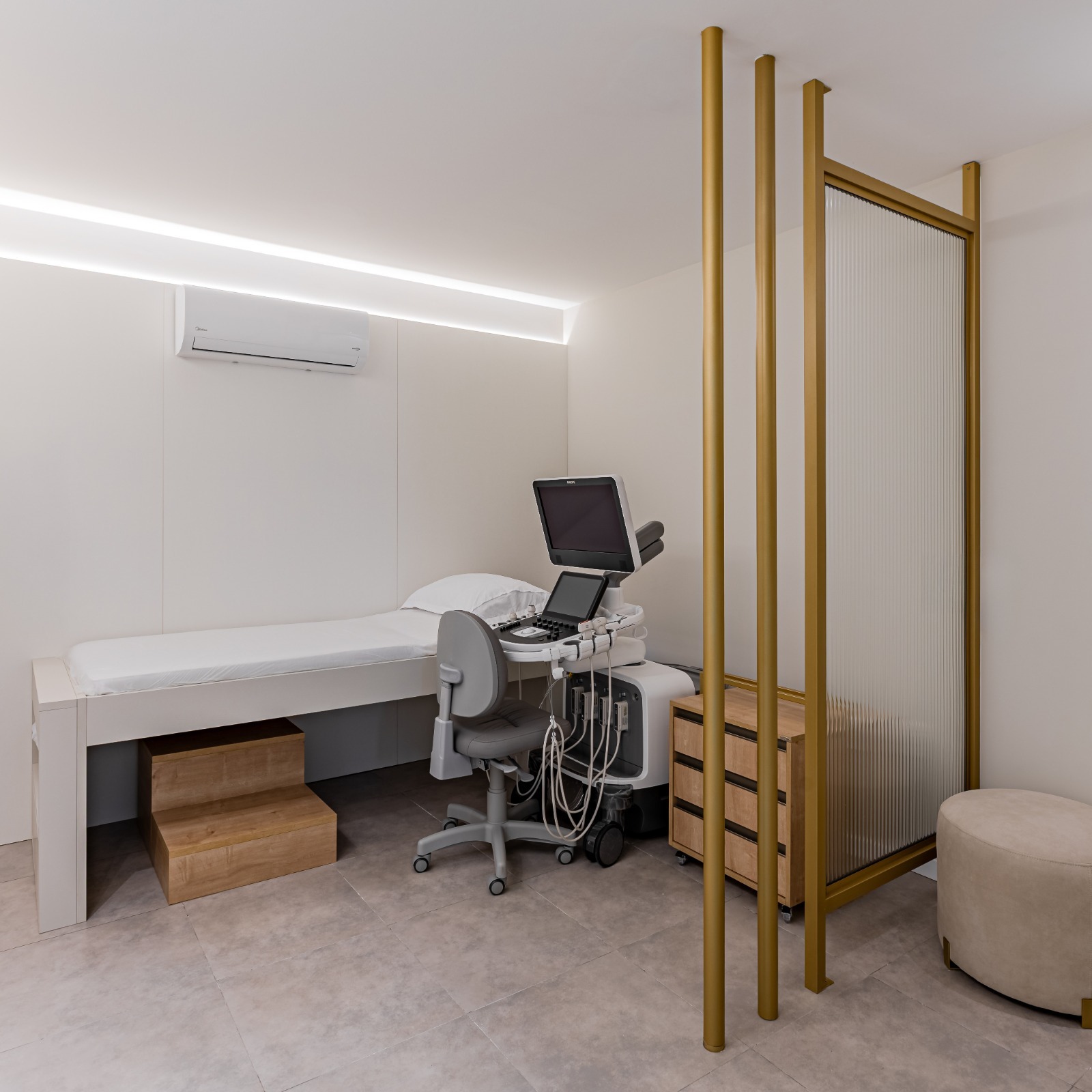 Sala de ecocardiografia com maca, aparelho de ultrassom e divisória dourada